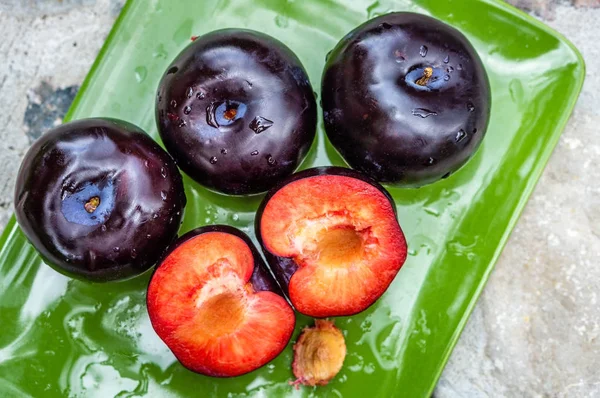 Tre mörklila plommon frukter och en klippa på en grön tallrik — Stockfoto