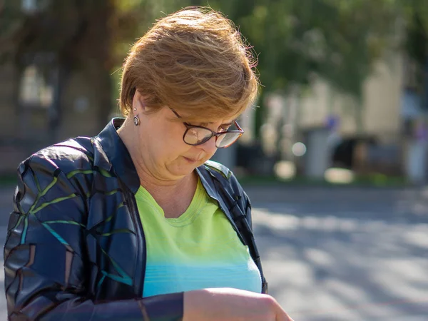 Femme mûre avec des lunettes marche dans les rues de la ville — Photo