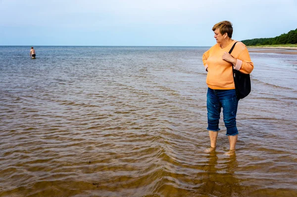 Pensativo Madura mujer en una chaqueta naranja deambula en el agua — Foto de Stock