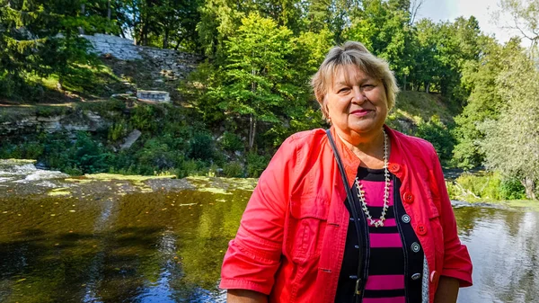 Mujer madura en una chaqueta roja descansando junto al río . — Foto de Stock