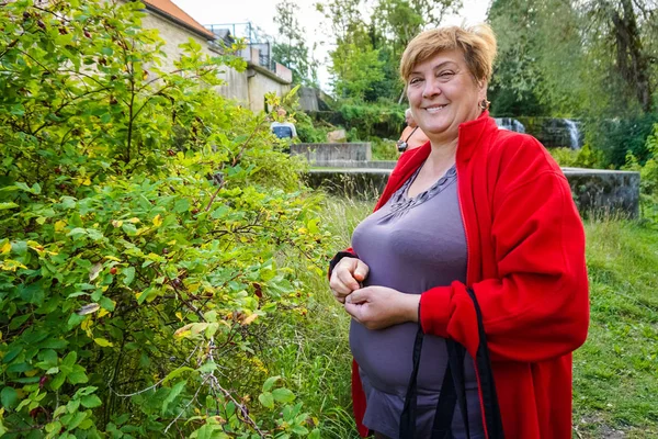 Mujer madura en una chaqueta roja descansando junto al río . —  Fotos de Stock