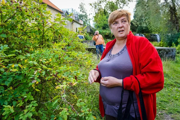 Mature woman in a red jacket resting by the river. — Stock Photo, Image