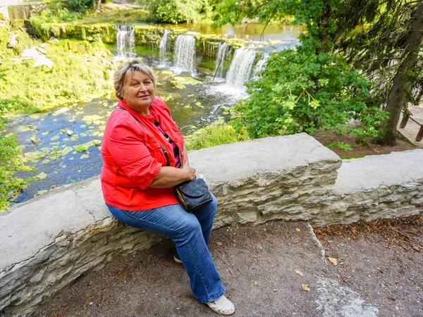 Volwassen vrouw in een rode jas rusten aan de rivier. — Stockfoto