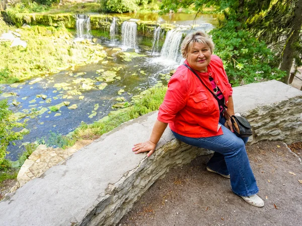 Mature woman in a red jacket resting by the river. — Stock Photo, Image