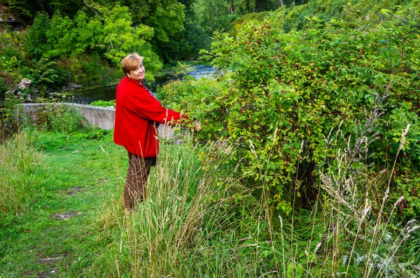 Starsza kobieta w czerwonej kurtce spoczywającej na rzece. — Zdjęcie stockowe