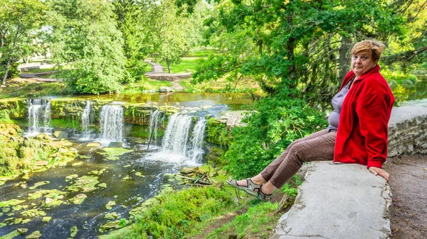Kırmızı ceketli olgun kadın nehir kıyısındaki Parkta dinleniyor.. — Stok fotoğraf