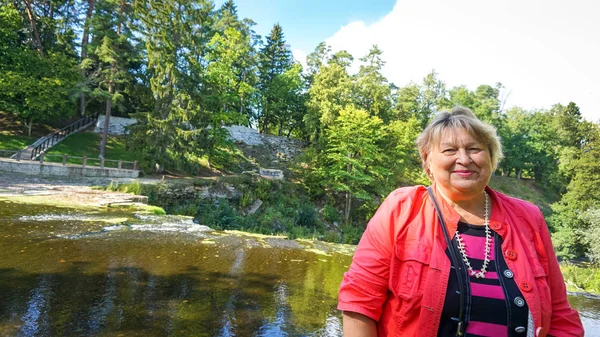 Mujer madura en chaqueta roja está descansando en el parque junto al río . — Foto de Stock