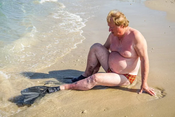 Un uomo anziano con le pinne appoggiato sulla spiaggia — Foto Stock