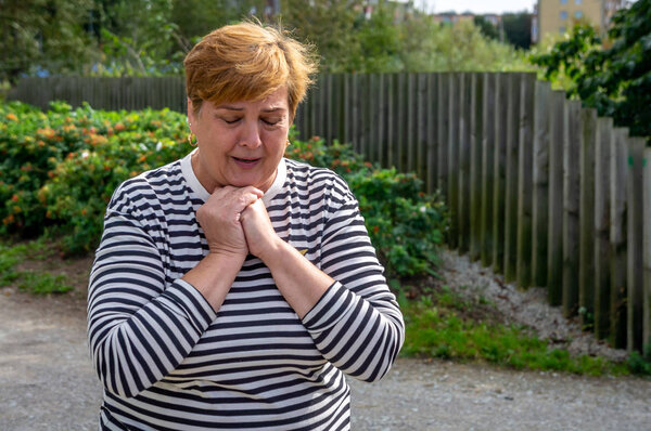 Зрелая женщина в полосатой рубашке гуляет в парке
