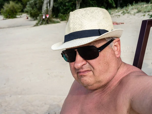 Brooding vieux grand-père dans les lunettes de soleil et chapeau bronzer sur bea — Photo