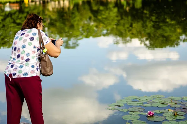 Mature woman takes pictures on a smartphone water Lily — Stock Photo, Image