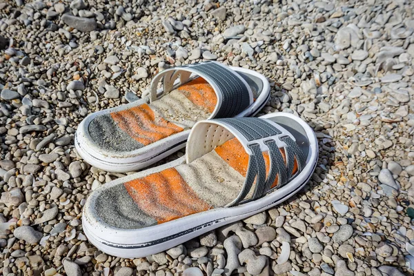 Zapomenuté plážové pantofle leží na oblázkech u moře — Stock fotografie