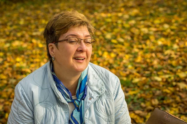 Mujer madura feliz descansando en el parque de la ciudad en otoño — Foto de Stock