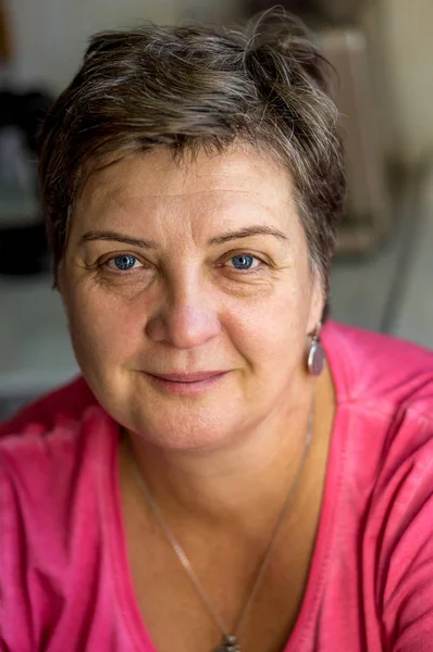 Mature woman in red sits at the window — Stock Photo, Image