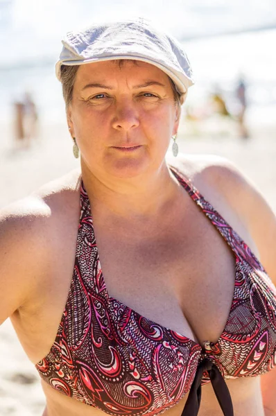 Volwassen vrouw in badpak en witte pet rusten door de zee — Stockfoto