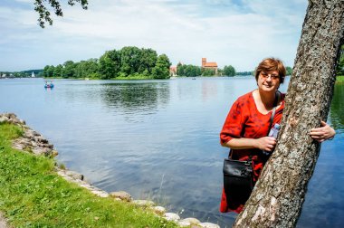 Kırmızı elbiseli olgun bir kadın gölün kenarındaki parkta yürüyor.