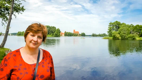 Kırmızı elbiseli olgun bir kadın gölün kenarındaki parkta yürüyor. — Stok fotoğraf