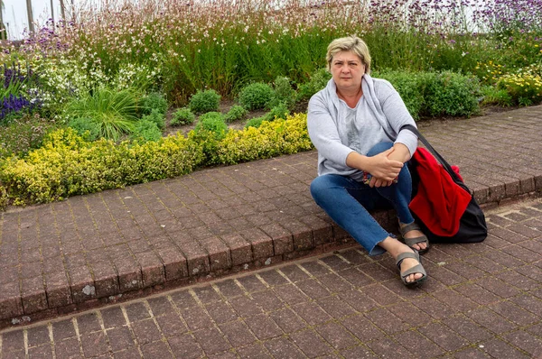 明るい熟女はカメラを見て微笑んだ 市内の休憩公園の花の庭に座って — ストック写真