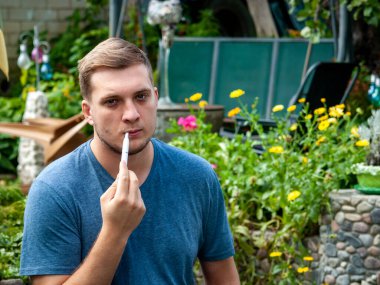 Traşsız adam bir sigara içiyor ve fotoğrafçıya bakıyor. Şehir parkında yürüyüş.