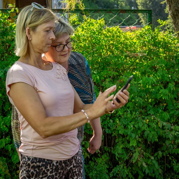 Dvě Krásné Ženy Procházející Parku Dívají Fotky Svém Mobilu — Stock fotografie