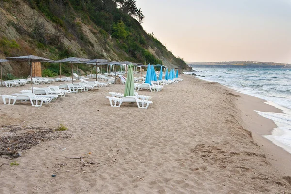 Deniz kenarında akşamları boş şezlong ve şemsiye ile günün sonunda boş kumsalda — Stok fotoğraf