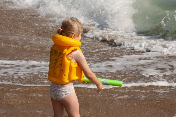 Chica joven con chaleco salvavidas amarillo. En la orilla con las olas . — Foto de Stock