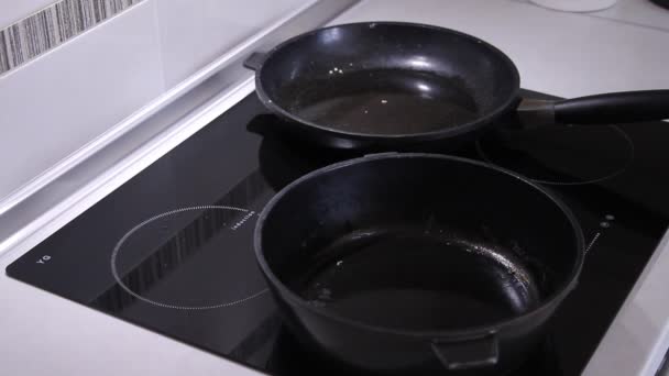 Two frying pans on an induction stove in which they pour the dough for pancakes — Stock Video