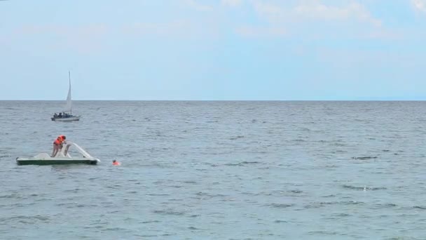 Katamaran mit Menschen auf dem Wasser und einer Jacht im Hintergrund. — Stockvideo