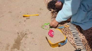 Bornozlu bir çocuk sahilde oyuncaklarla oynuyor.