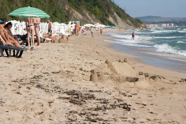 Uma praia com turistas no mar negro e um castelo de areia em primeiro plano. — Fotografia de Stock