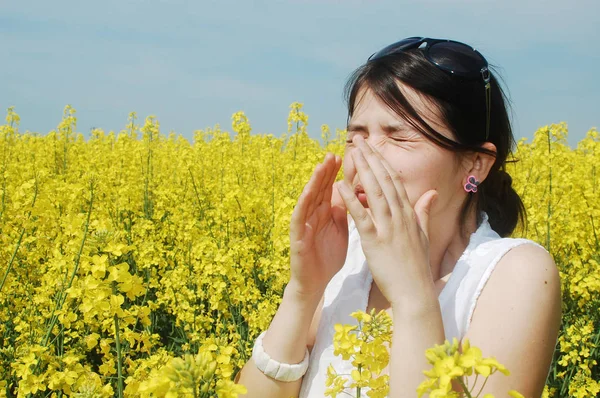Young woman sneezing in a field of flowers because of a pollen allergy