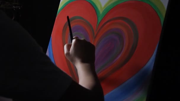 关闭女艺术家画一个大的红色心脏在她的工作室在黑暗的黑色背景的画架上 — 图库视频影像