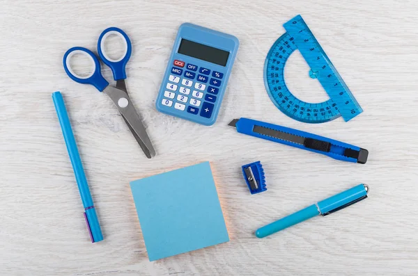 Electronic calculator, scissors, protractor, sharpener, cutter, pencil, pen and paper block on wooden table. Top view