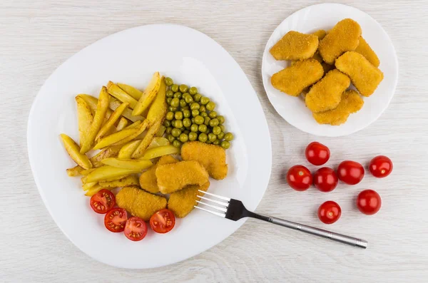 Fried potatoes, vegetables, chicken nuggets in plate, plate with chicken nuggets on wooden table. Top view