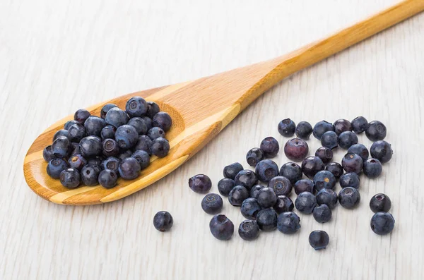 Blueberries on bamboo spoon, scattered blueberry on wooden table