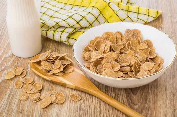 Multi cereal flakes in bowl, bamboo spoon with flakes, napkin, bottle of yogurt on wooden table
