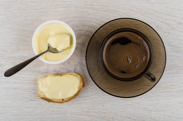 Sweet melted cheese, spoon in jar, sandwich with cheese, coffee in cup on wooden table. Top view