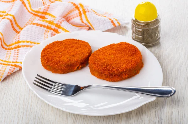 Cutlets in breading, fork in white dish, pepper, checkered napkin on wooden table