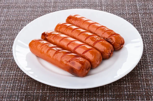 Few grilled sausages in white plate on dark mat