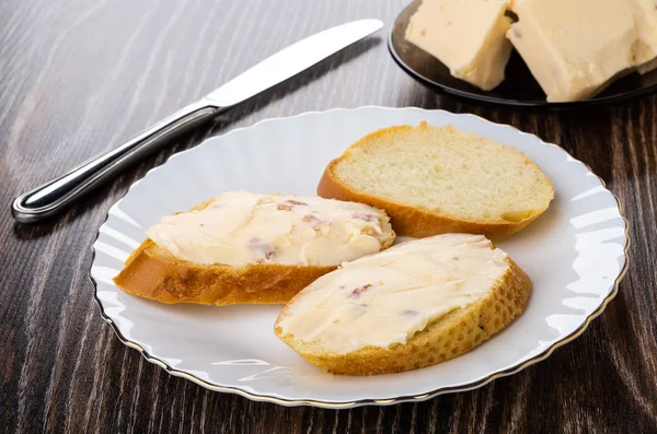 Pieces of melted cheese with bacon in plate, table knife, sandwiches with cheese in plate on wooden table