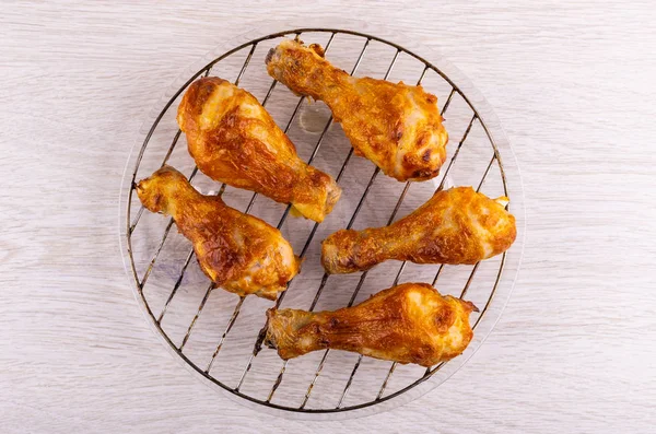 Fried chicken legs on grill in transparent plate on wooden table. Top view