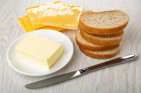Pieces of bread, packages of melted cheese, saucer with butter, table knife on wooden table