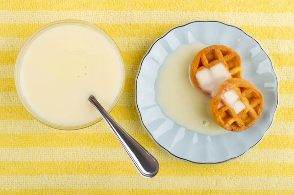 Soft waffles with condensed milk in saucer, bowl with condensed
