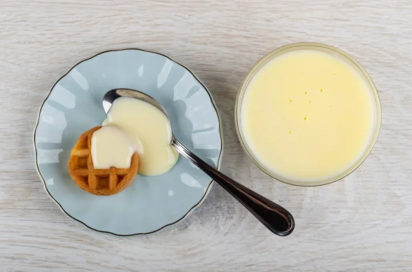 Bowl with condensed milk, round waffle, teaspoon with condensed