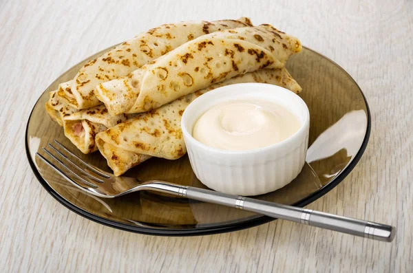 Fried pancakes roll with filling, bowl with mayonnaise, fork in