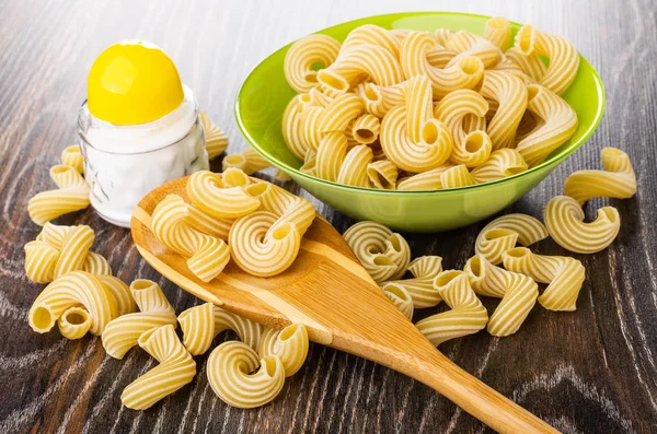 Green bowl with raw pasta cavatappi, macaroni in spoon, salt sha