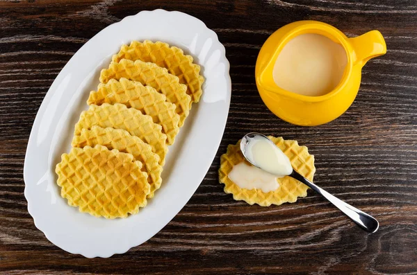 Dish with cookies, condensed milk in spoon on cookie, pitcher wi