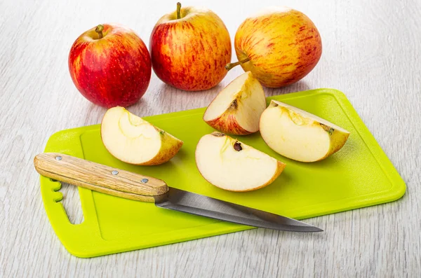 Red apples, halves of apples, knife on cutting board on wooden t