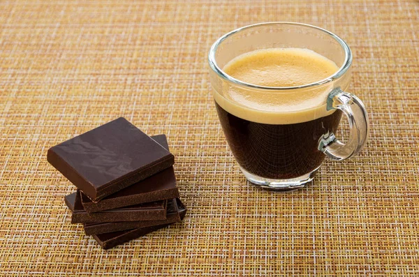 Stack of pieces of chocolate, cup with coffee espresso on mat