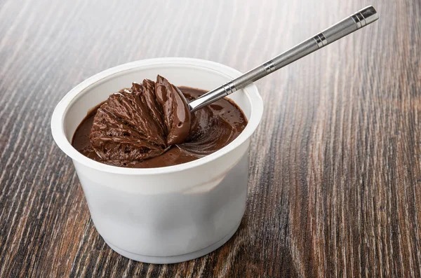 Spoon with chocolate melted cheese in white jar on table